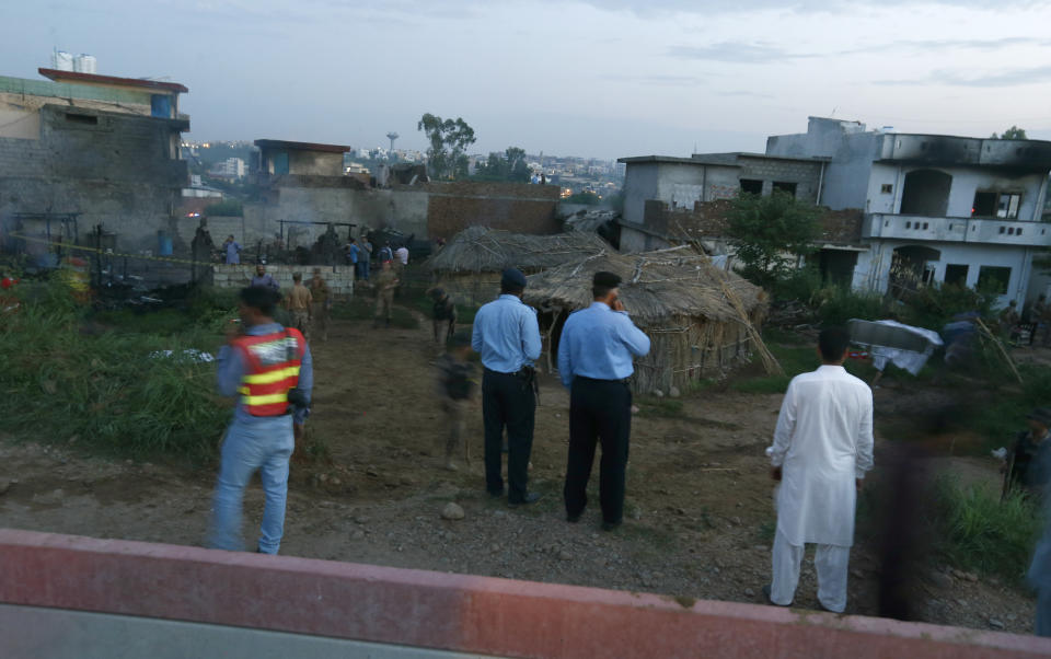 Pakistan army troops and police officer gather the site of plane crash in Rawalpindi, Pakistan, Tuesday, July 30, 2019. A small Pakistani military plane crashed into a residential area near the garrison city of Rawalpindi before dawn, killing some people, officials said. (AP Photo/Anjum Naveed)