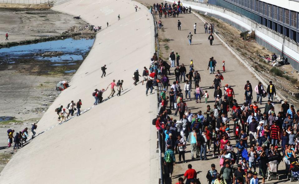 <p>Migrants climb up a bank of the nearly dry Tijuana River as they make their way around a police blockade toward the El Chaparral port of entry on November 25, 2018 in Tijuana, Mexico.</p>