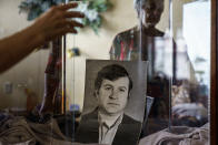 Lyubov Mahlii, 76, reaches for a photo of her late husband, Nikolai, in her apartment in Sloviansk, Donetsk region, eastern Ukraine, Saturday, Aug. 6, 2022. Following the death of her husband from diabetes four years ago, Mahlii shares her Soviet government-provided apartment with two bright yellow canaries and an assortment of houseplants. (AP Photo/David Goldman)