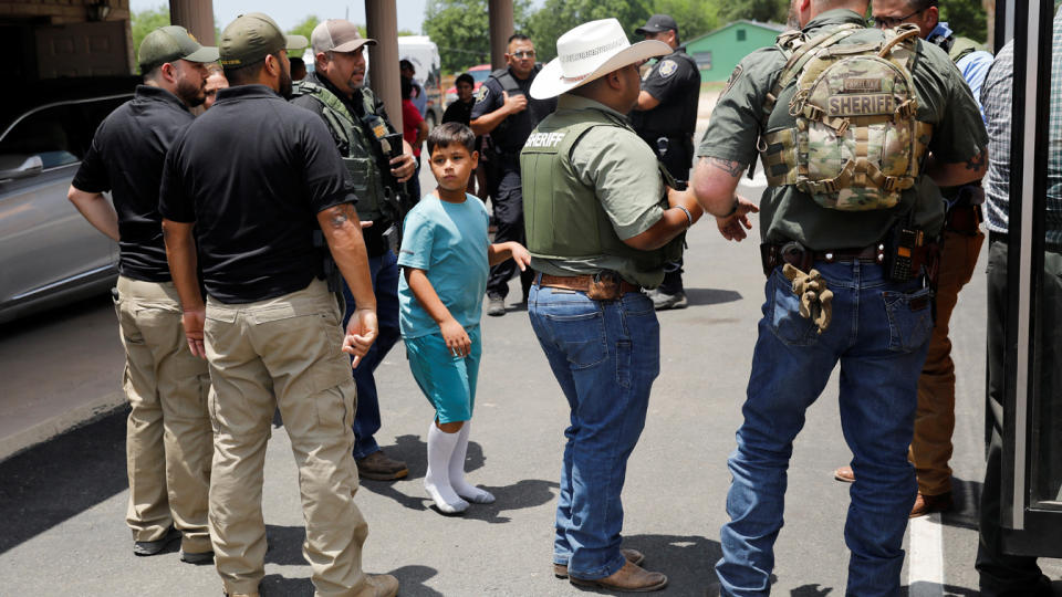 A child gets on a school bus as law enforcement personnel guard the scene of the Uvalde mass shooting. 
