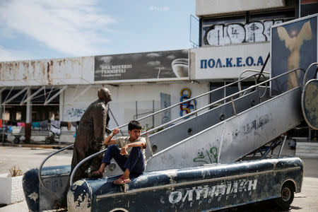 A boy sits next to an old statue outside the main building of the disused Hellenikon airport where stranded refugees and migrants, most of them Afghans, are temporarily accommodated in Athens, Greece, May 3, 2016. REUTERS/Alkis Konstantinidis