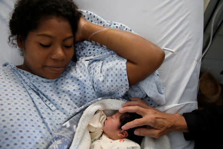 Honduran migrant Alvin Reyes, 39, touches his newborn son Alvin, next to his wife Erly Marcial, 21, at a hospital in Puebla, Mexico, November 13, 2018. REUTERS/Carlos Garcia Rawlins