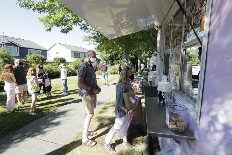Julie and Greg Schwab wait to order from the Dreamy Drinks food truck, Monday, Aug. 10, 2020, near the suburb of Lynnwood, Wash., north of Seattle. In June, Julie Schwab started organizing a regular schedule to bring food trucks to their neighborhood as a way to both help small businesses and give families staying at home during the coronavirus pandemic different options for meals. Long seen as a feature of city living, food trucks are now finding customers in the suburbs during the coronavirus pandemic as people are working and spending most of their time at home. (AP Photo/Ted S. Warren)