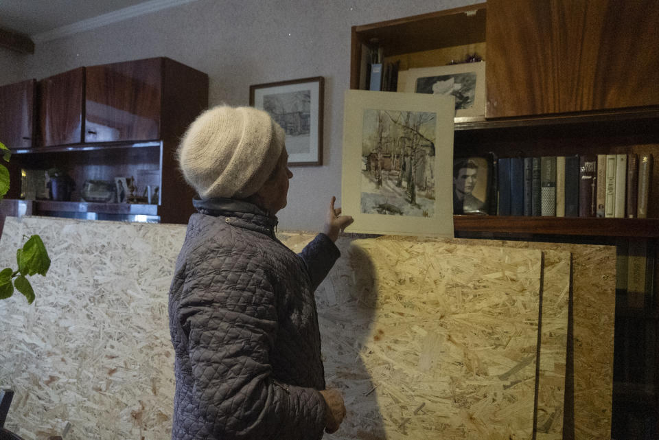 Liudmyla, 78, Mykola's Soloviov wife, holds up her husband's painting of the landscapes seen from the window in the room of their apartment damaged by a missile attack in Sloviansk, a city in Donetsk region, his hometown which lies 25 kilometers from the frontline, Ukraine, Saturday, Jan. 27, 2024. Soloviov, 88, is a painter the world does not know. His expressive and imaginative landscapes of eastern Ukraine encapsulate a lost time, and lie undiscovered, tucked away in a modest home under threat of Russian attack. (AP Photo/Vasilisa Stepanenko)