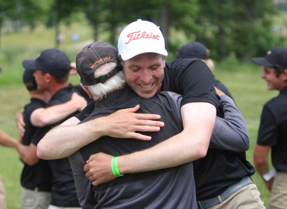 Northville head coach Matt Lewicki (right) embraces assistant coach John Balagna after learning the Mustangs won the state Division 1 golf tournament Saturday, June 10, 2023 at The Meadows in Allendale.