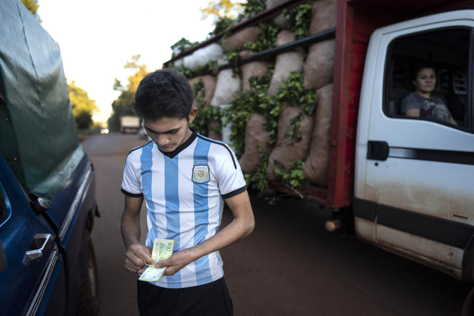 Fabián Acuña, que viste la casaca de la selección argentina de fútbol, cuenta su paga semanal por la cosecha de yerba mate fuera de su casa, donde el capataz llegó en su camión para dejarle su salario en Andresito, en la provincia argentina de Misiones, el viernes 19 de abril de 2024. Ricos o pobres, de izquierda o de derecha, fanáticos del Boca Juniors o de su acérrimo rival futbolístico, el River Plate, a los argentinos les encanta el mate. (AP Foto/Rodrigo Abd)