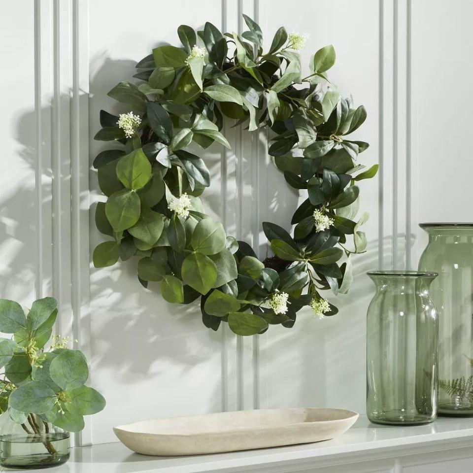 Decorative green leaf wreath on a wall beside a glass vase and bowl on a shelf