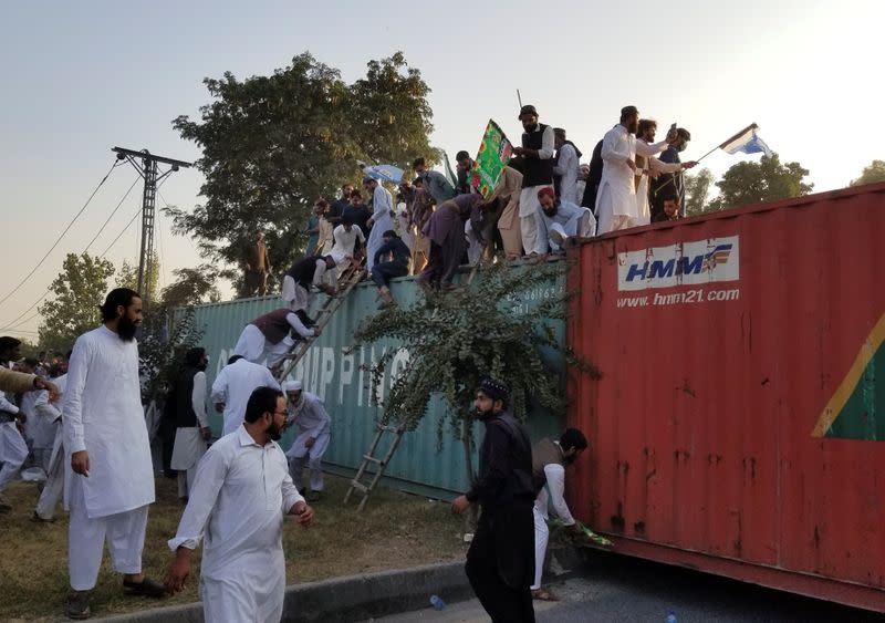 People climb over shipping containers as they try to go towards the French Embassy during a protest against the cartoon publications of Prophet Mohammad in France, in Islamabad