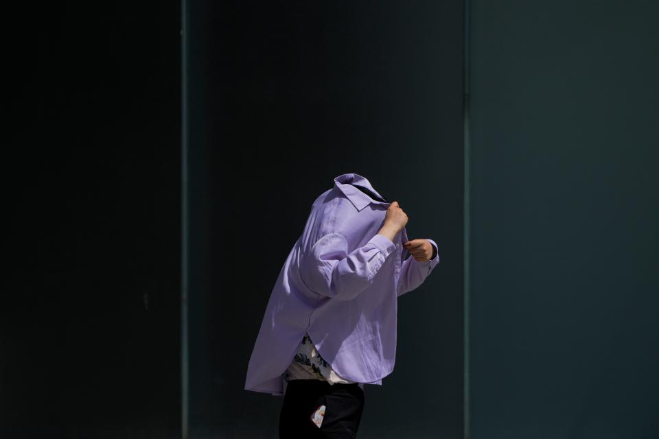 A woman uses a long-sleeve shirt to shield from the sun as she walks at an outdoor shopping mall on a sweltering day in Beijing, Thursday, July 6, 2023. Employers in Beijing were ordered Thursday by the government to stop outdoor work after scorching summer heat in the Chinese capital was forecast to reach 40 degrees centigrade (104 Fahrenheit).