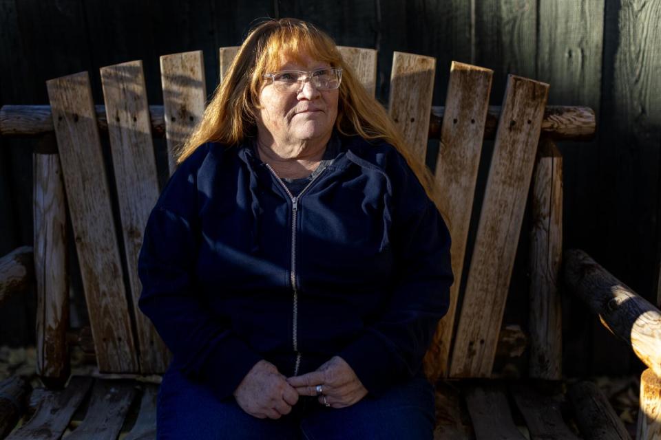 A woman with long red hair sits on a wooden bench.