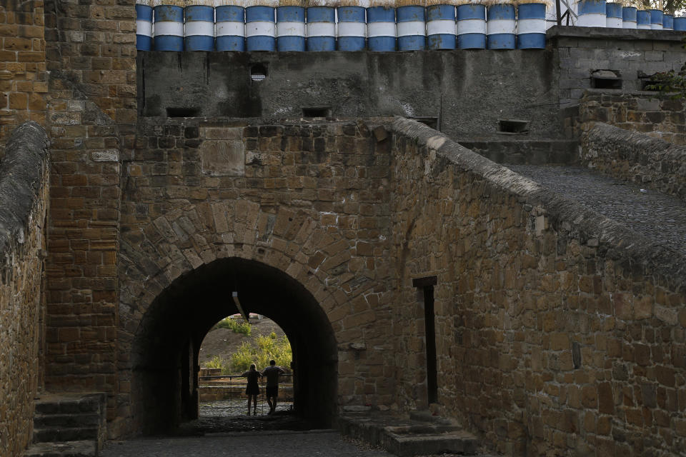 A couple stand inside Paphos gate with the barrels on the top, used from Cyprus' military at an abandoned military guard post in divided capital Nicosia, Cyprus, Saturday, April 24, 2021. United Nations Chief Antonio Guterres is to host in Geneva between April 27-29 an informal gathering of the rival Greek Cypriot and Turkish Cypriot leaders in the hope of prompting new reunification talks. (AP Photo/Petros Karadjias)