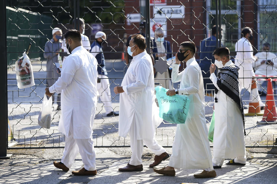 People wearing face masks arrive before having their temperatures checked to try stop the spread of coronavirus, before being allowed to go into Manchester Central Mosque, in Manchester, northern England, as Muslims worldwide mark the start of the Eid al-Adha holiday, Friday, July 31, 2020. The British government on Thursday night announced new rules on gatherings in some parts of Northern England, including Manchester, that people there should not mix with other households in private homes or gardens in response to an increase trend in the number of cases of coronavirus cases per 100,000 people. (AP Photo/Jon Super)