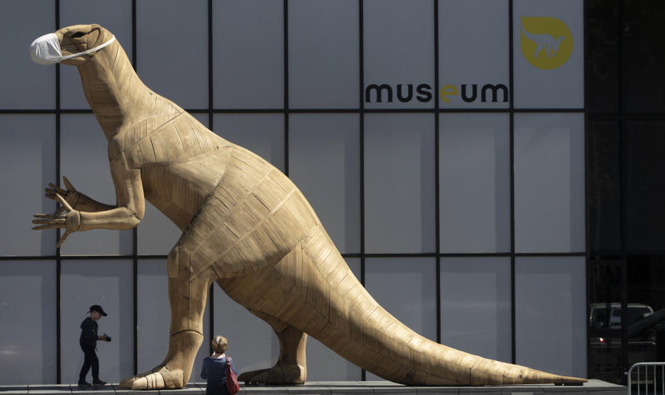 A boy walks by a model of a dinosaur wearing a face mask, during a partial lockdown to prevent the spread of the coronavirus, at the Museum of Natural History in Brussels, Tuesday, May 19, 2020. Museums are hesitantly starting to reopen as the coronavirus lockdown measures are relaxed, yet experts say that one in eight in the world could potentially face permanent closure because of the pandemic. (AP Photo/Virginia Mayo)