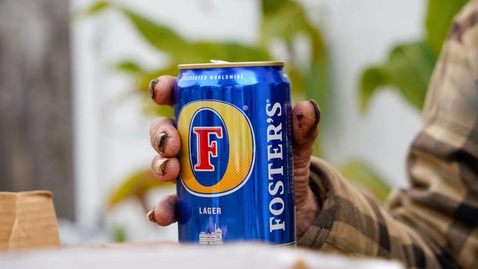 Cowboy, an unhoused resident of Shell Beach, holds a can of Foster’s beer. Cowboy has been homeless for more than 25 years but said he isn’t interested in being housed.