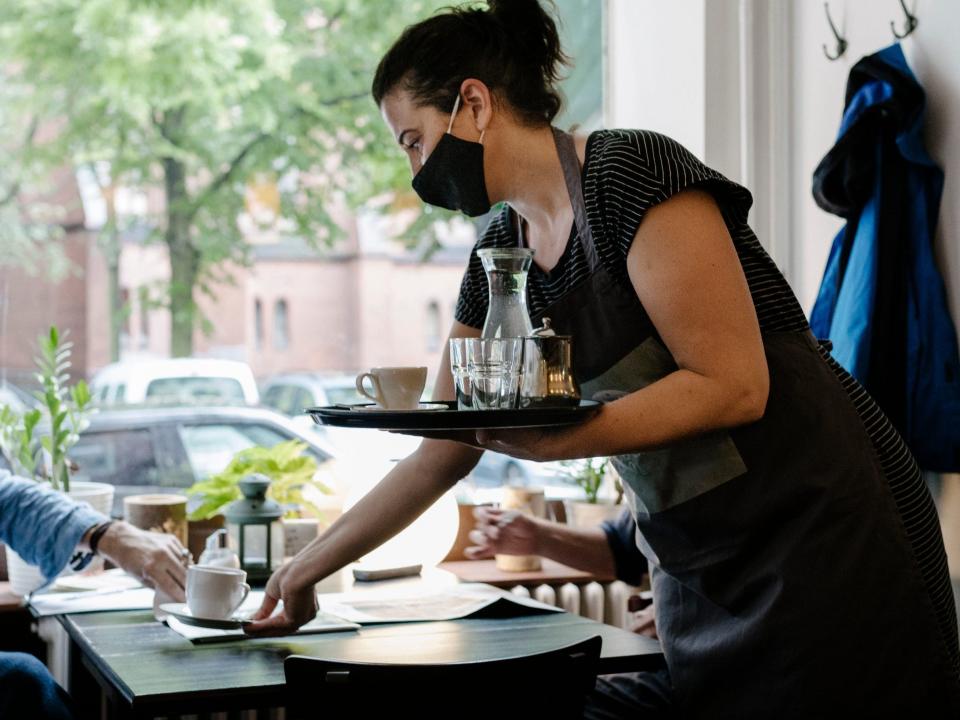 A waitress wearing a face mask and serving a customer some coffee at his table in a restaurant.