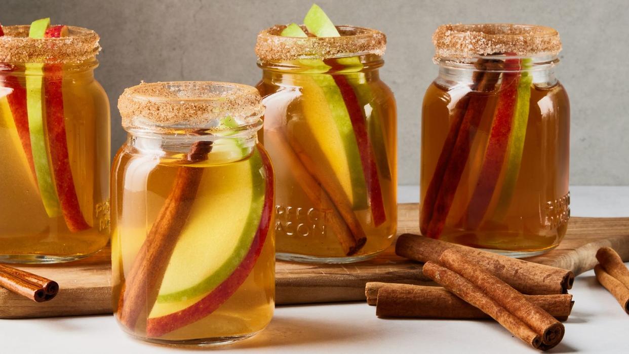 apple pie bourbon shots with apple slices and cinnamon sticks in little mason jars