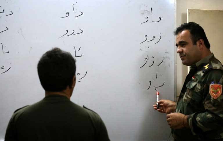 An Iraqi Kurdish peshmerga fighter teaches his fellow comrades to read during a class at a school in the northern Iraqi village of Bahra, on June 16, 2015