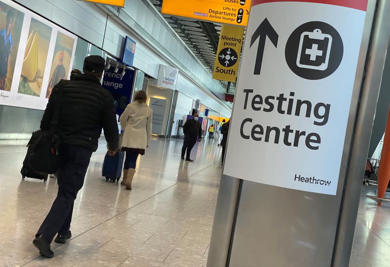 Travellers pass a sign for a COVID-19 test centre at Heathrow Airport