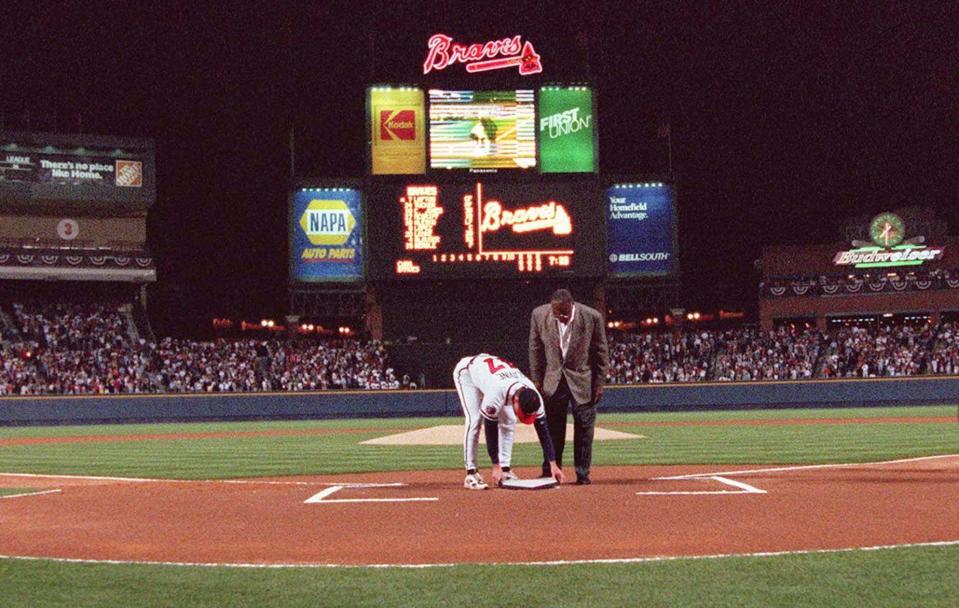 FILE - In this April 4, 1997, file photo, former Atlanta Braves great Hank Aaron looks on as pitcher Tom Glavine places down home plate from Atlanta Fulton County Stadium on top of the plate at Turner Field before the Braves opened their new home against the Chicago Cub in Atlanta. To baseball fans, opening day is an annual rite of spring that evokes great anticipation and warm memories. This year's season was scheduled to begin Thursday, March 26, 2020, but there will be no games for a while because of the coronavirus outbreak. (AP Photo/John Bazemore, File)