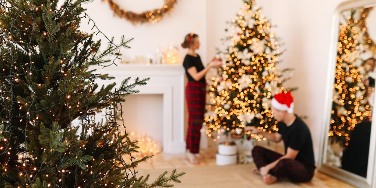 a happy couple in love in pajamas are preparing for the holiday, celebrating christmas and new year by decorating a christmas tree in the cozy interior of the house in winter in december