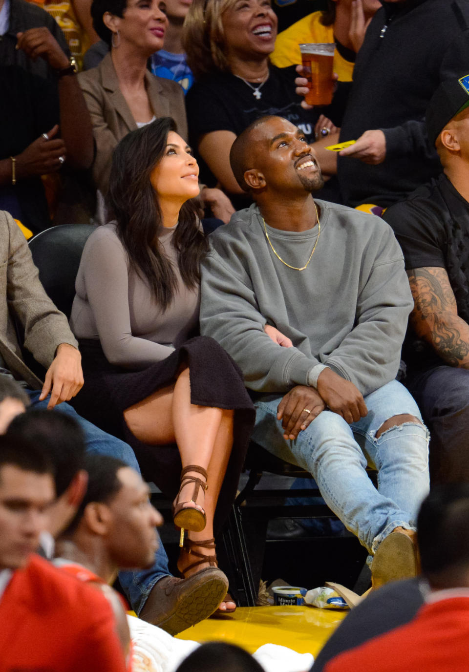 True to form, Kim Kardashian rocks ridiculously high heels — in a setting that calls for sneakers — a skirt with a high slit, and tight shirt. Her hubby is more casual, but there’s no doubt that his crewneck sweatshirt and strategically ripped jeans cost more than seats. 