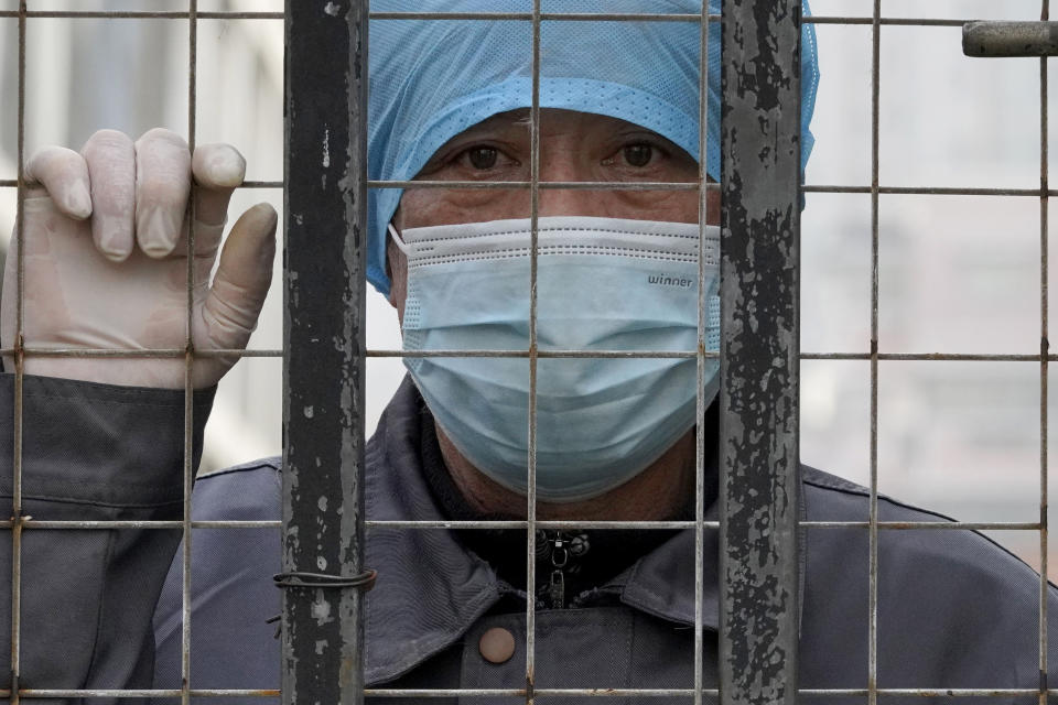 A worker wearing a mask, watches from inside a hospital across the Wuhan Center for Disease Control and Prevention after the World Health Organization team arrive to make a field visit in Wuhan in central China's Hubei province on Monday, Feb. 1, 2021. (AP Photo/Ng Han Guan)