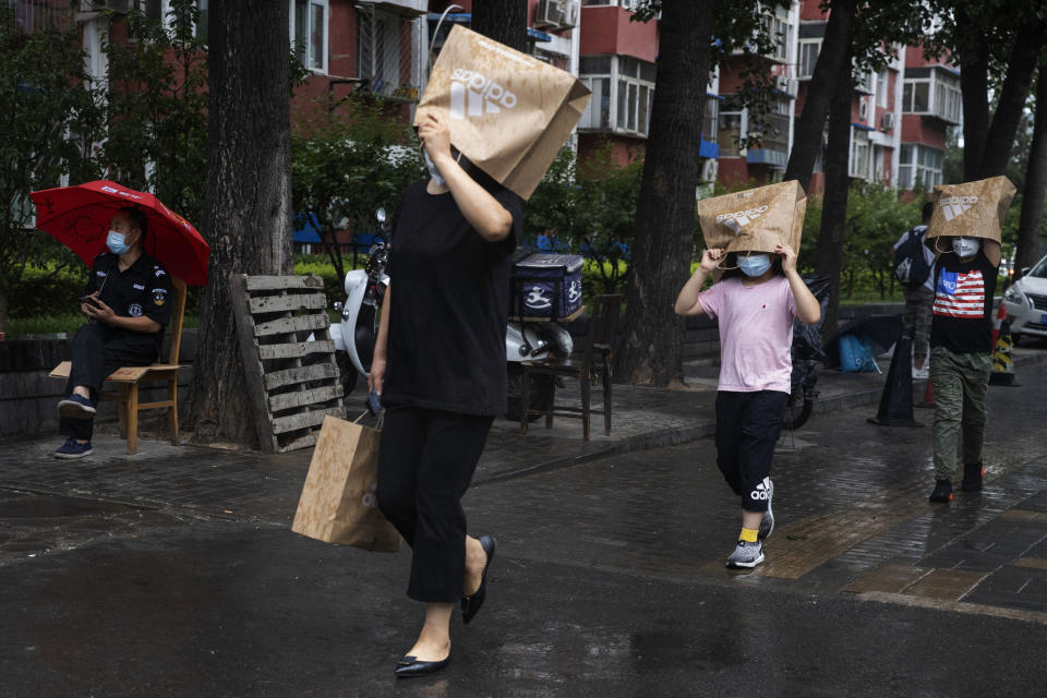 Residents wearing face masks to curb the spread of the coronavirus hold up paper bags to protect against the rain in Beijing on Thursday, June 18, 2020. A new coronavirus outbreak in Beijing saw a decline in daily cases Thursday while the United States increased pressure on China's leaders to reveal what they know about the pandemic. (AP Photo/Ng Han Guan)