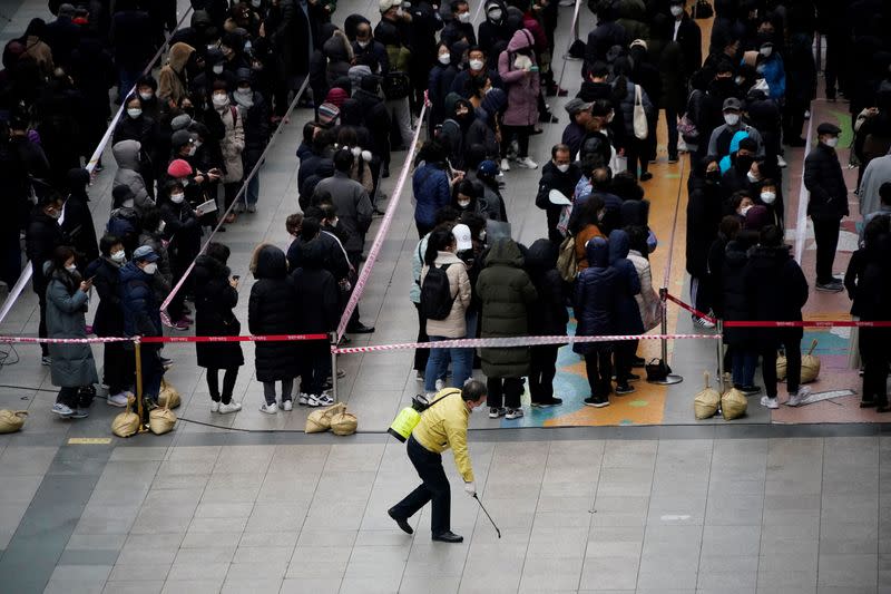 People wearing masks after the coronavirus outbreak wait in a line to buy masks as a government official sanitizes the floor in front of a department store in Seoul