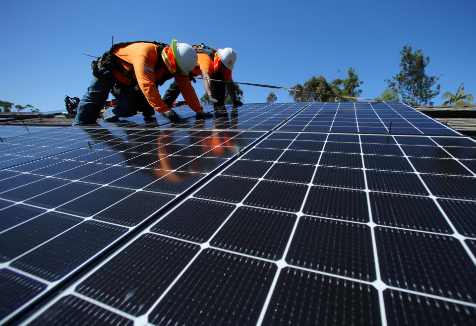 Workers in hard hats on a roof, installing solar panels.