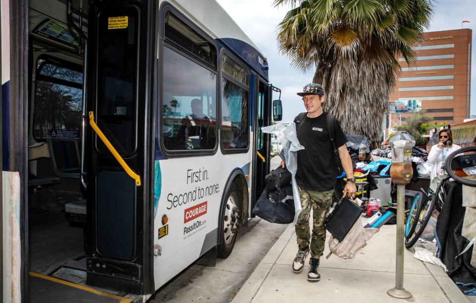 A man carrying a backpack, tote bags and bedding boards a bus.