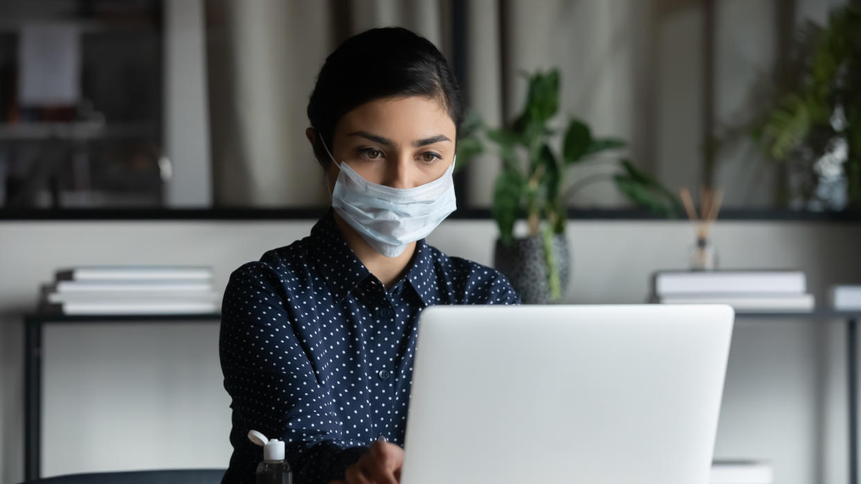 Concentrated young female indian professional wearing breath protective mask, working on computer after washing hands with antiseptic liquid, preventing spreading coronavirus infection in office.Working from home has created a whole new issue around online security. Here's how to protect yourself. (Photo: Getty)