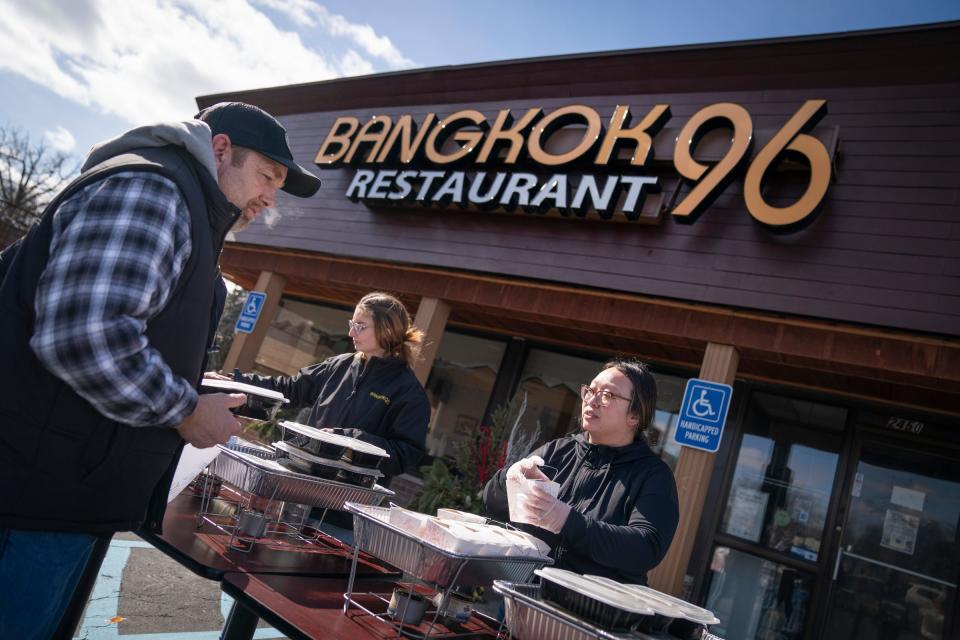 James Ferns, 54, of Dearborn Heights, left, who has been without power for days was delighted to pick up some freshly cooked Thai food after chef and owner of Bangkok 96 in Dearborn, Genevieve Vang, and her staff, also without power, emptied their restaurant coolers on Friday, Feb. 24, 2023 to cook food in a giant wok with propane tanks and present the food to the community for free. "The community supported us through COVID," said Vang's daughter Christine Vang, 27, right. "This is our opportunity to pay them back," she added. Ferns commented: "It's awesome they not wasting nothing. ...I am so appreciative of this."