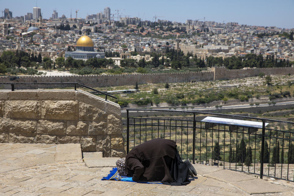 A Muslim woman wears gloves prays in east Jerusalem's Mount of Olives, overlooking the Dome of the Rock and al-Aqsa mosque compound, which remains shut to prevent the spread of coronavirus during the holy month of Ramadan, Friday, May 1, 2020. (AP Photo/Ariel Schalit)