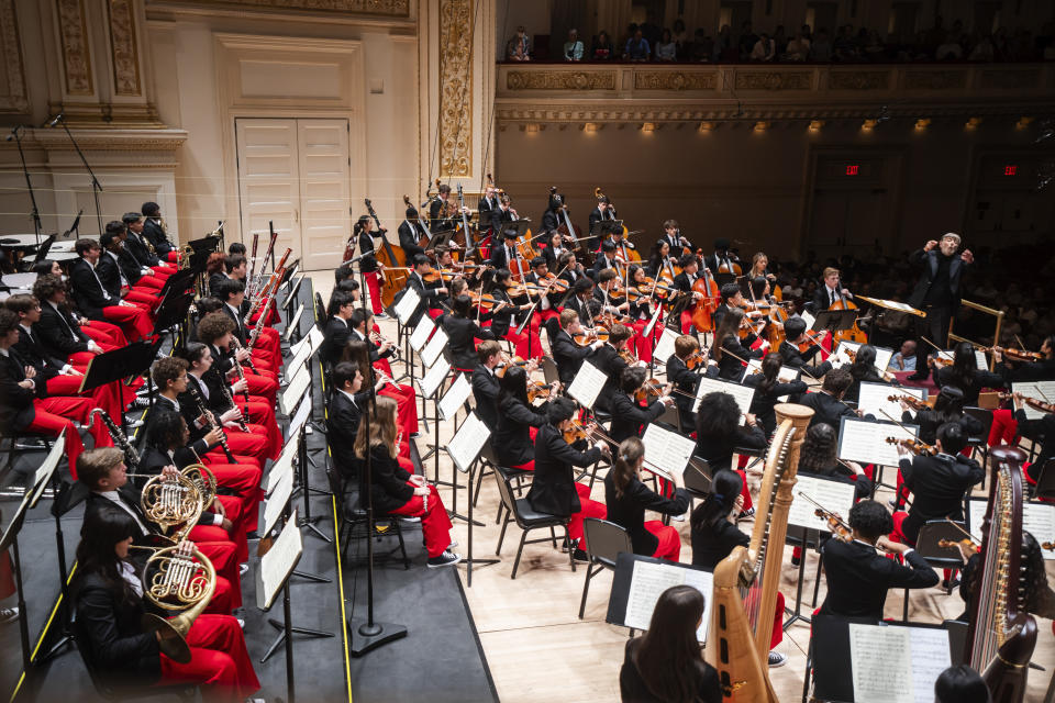 This image provided by the Carnegie Hall shows the National Youth Orchestra of the USA being led by Sir Andrew Davis, right. Teenaged musicians from the National Youth Orchestra of the USA walked onto the Carnegie Hall stage before rehearsal and had a uniform reaction, much like string sections following their leaders: They pulled out cell phones and took selfies. Carnegie Hall's initiative to train the next generation turned 10 this year. (Chris Lee/Carnegie Hall via AP)