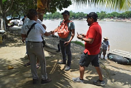 Agent of the National Migration Institute checks the IDs of people who have crossed the Suchiate River on a raft from Tecun Uman, Guatemala, to Ciudad Hidalgo, as seen from Ciudad Hidalgo