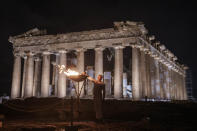 Retired Greek 400-meter hurdles champion Periklis Iakovakis lights a cauldron with the Olympic flame in front of the ancient Parthenon temple at the Acropolis hill, Friday, April 19, 2024. The flame that will burn at the summer Olympics is spending the night at the ancient Acropolis in Athens, a week before its handover to Paris 2024 organizers. (AP Photo/Petros Giannakouris)