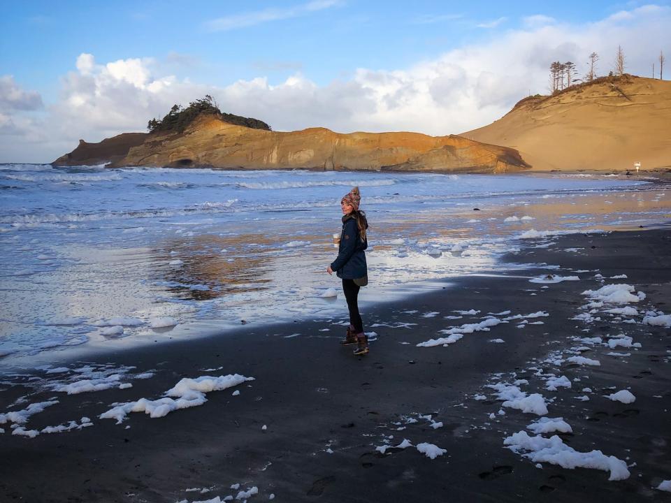 Emily on a beach with snow. There are small mountains in the background.