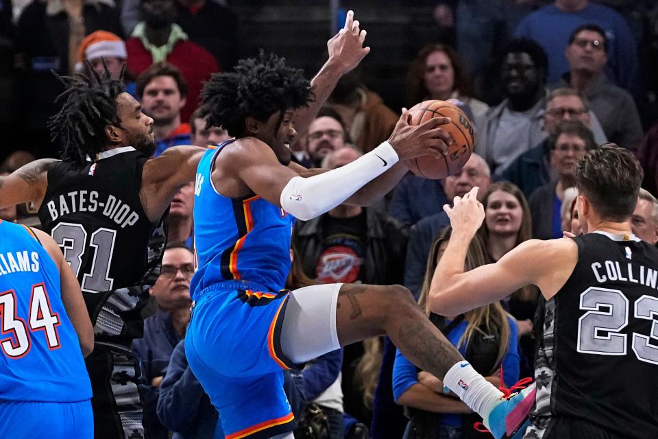 Oklahoma City Thunder forward Jalen Williams, center, grabs a rebound between San Antonio Spurs forward Keita Bates-Diop (31) and forward Zach Collins (23) during the second half of an NBA basketball game Wednesday, Nov. 30, 2022, in Oklahoma City. (AP Photo/Sue Ogrocki)