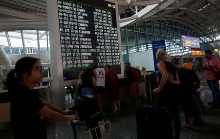 Passengers stand near the flight information board after Indonesian and regional authorities heightened flight warnings, following the eruption of Bali's Mount Agung volcano at Ngurah Rai International airpot in Bali, Indonesia, November 26, 2017. REUTERS/Nyimas Laula