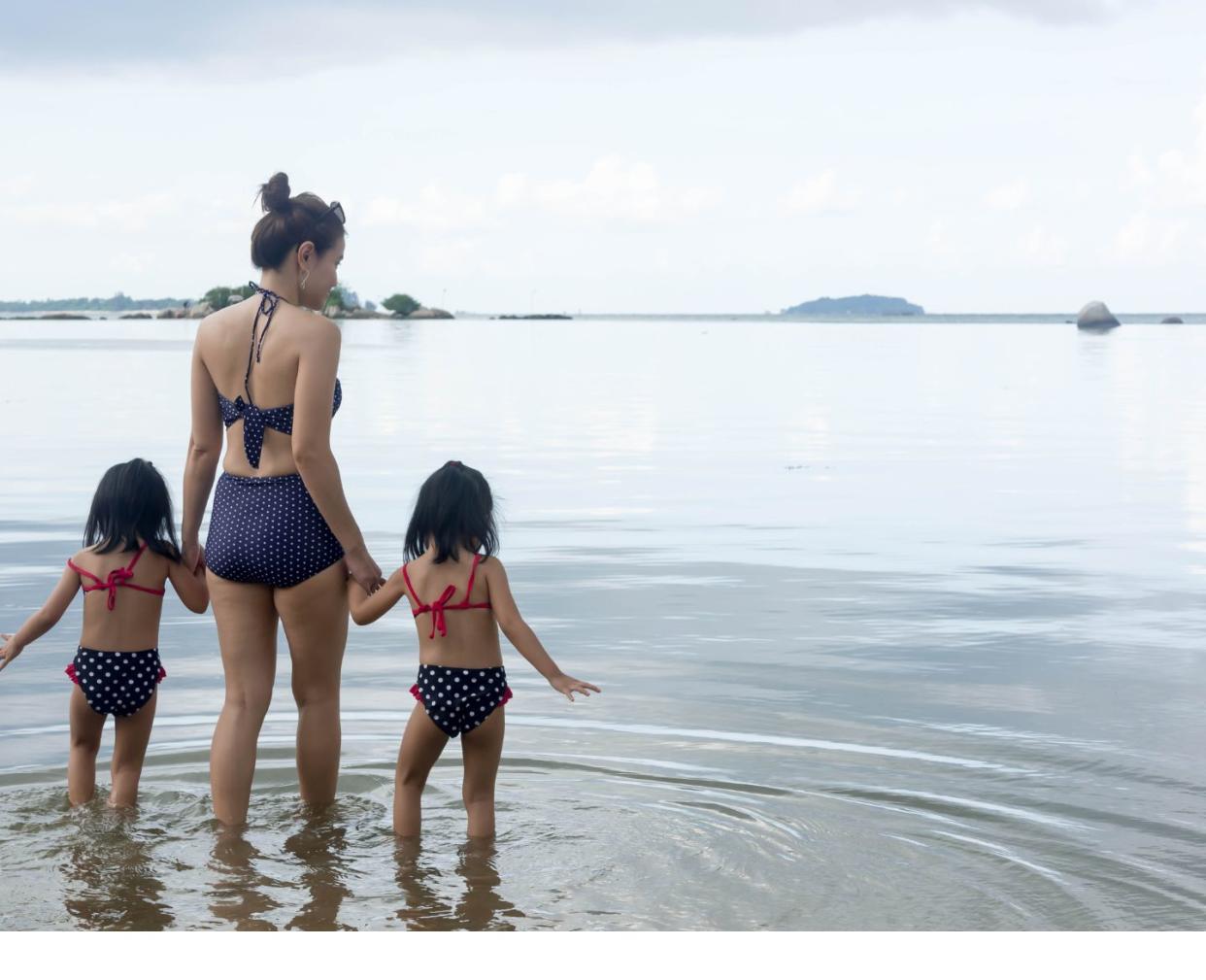 mom in swimming suit on beach with young daughters