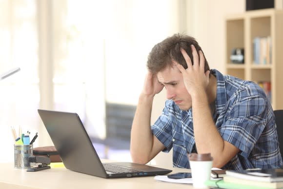 Young male at laptop holding his head and looking upset