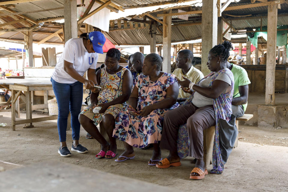 Rita Quansah, left, from Uniti Networks, coaches farmers on how to navigate its platform of applications, from pensions that encourage saving to agriculture apps, at a market in Hohoe, Ghana, Wednesday, April 18, 2024. Internet-enabled phones can play a unique role in sub-Saharan Africa, where infrastructure and public services are among the world’s least developed. But despite growing mobile internet coverage on the continent of 1.3 billion people, just 25% of adults in sub-Saharan Africa currently have access to it. (AP Photo/Misper Apawu)