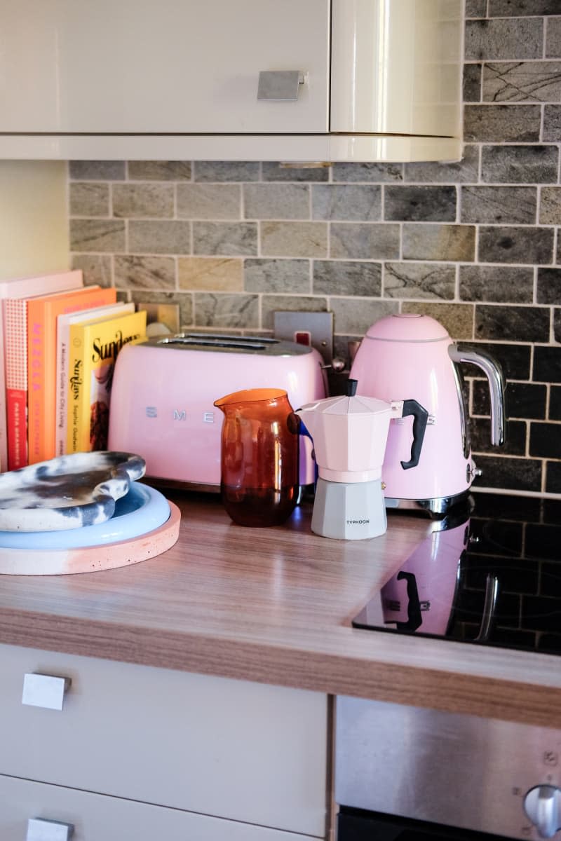 Pink small appliances sit on countertop of white kitchen.