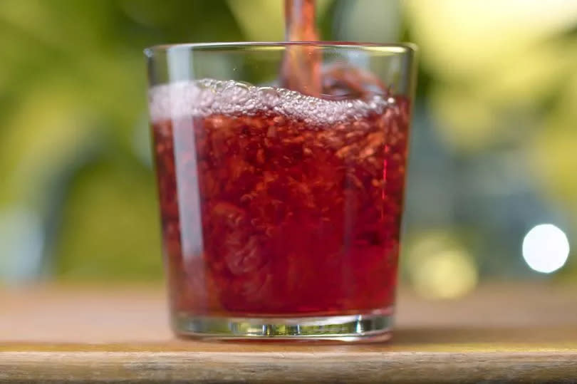 Red transparent juice or wine pouring into the glass with splashes and bubbles against natural green background. Close up cherry or pomegranate or cranberry juice or wine. Healthy eating concept.