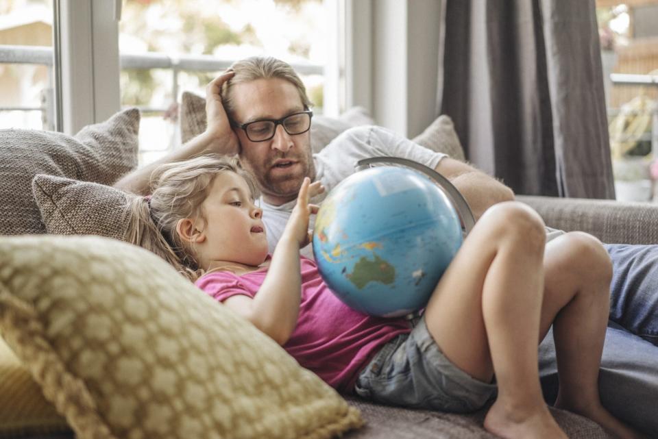 Father and daughter lying with globe on sofa