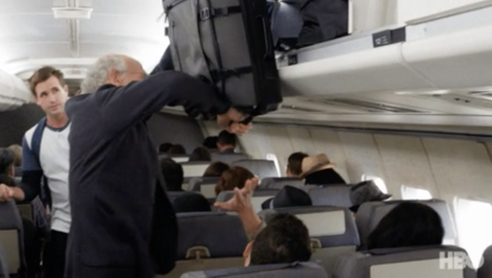 A scene from Curb Your Enthusiasm of a suitcase being put into the overhead bin