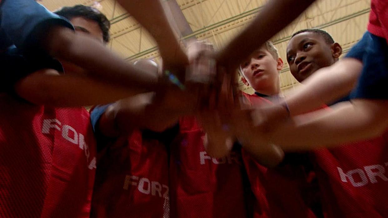 Donning red pinnies, a group of Saint Mary's Academy students put their arms together as they prepare to play a game of futsal, a variation of soccer that can be played indoors.  (Radio-Canada - image credit)
