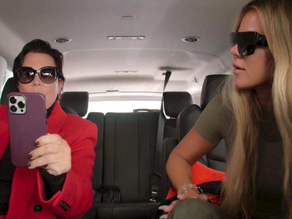 kris jenner and khloé kardashian in the backseat of a large car, both wearing sunglasses. kris is holding up her phone, as if she's calling someone