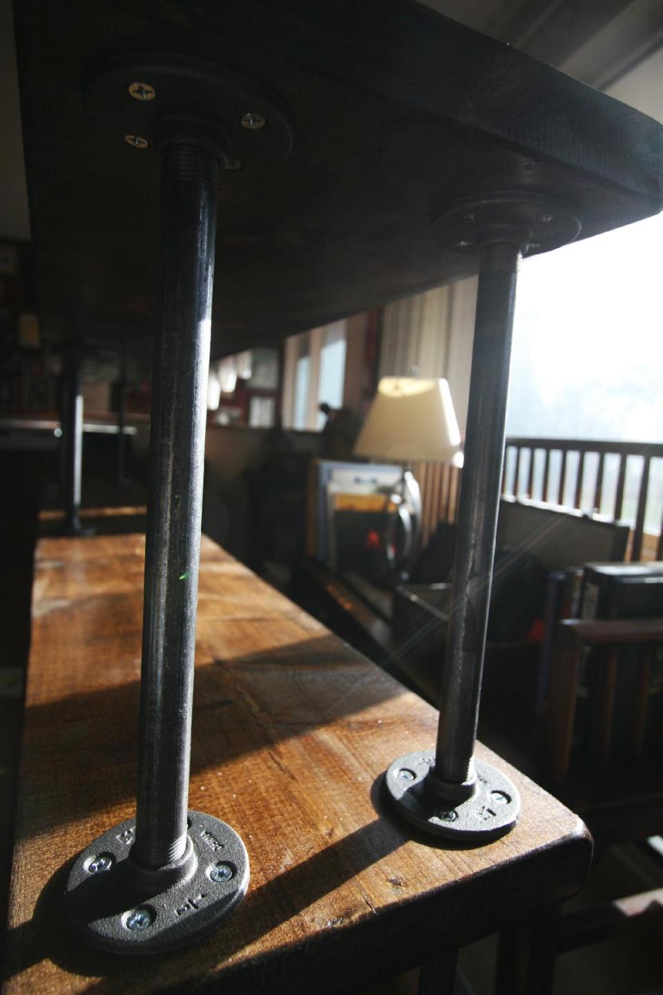 This undated photo shows the creation of a DIY bookshelf beginning with attaching pipes to the flanges on the shelf and under the shelve above. Using this same process, you can add as many levels to your bookshelf as you wish. (AP Photo/Ted Anthony)