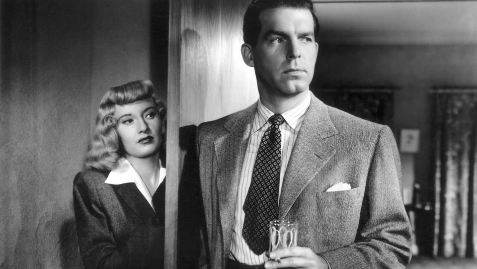 Barbara Stanwyck hides behind a door as Fred MacMurray holds a drink in Double Indemnity.